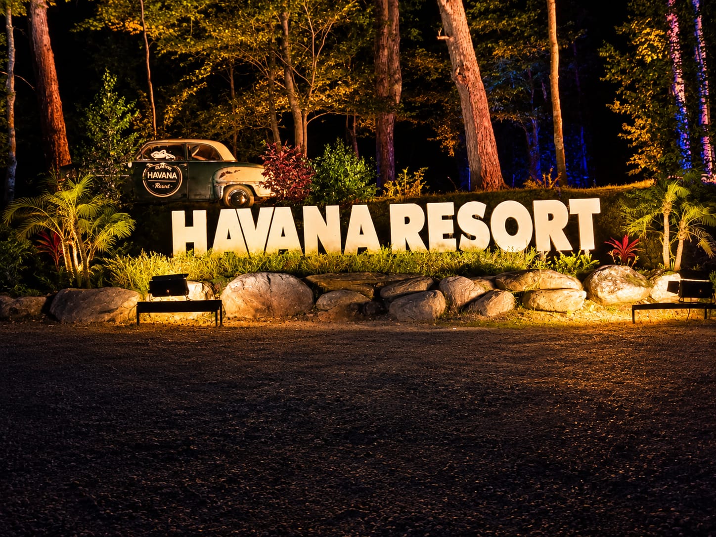 Enseigne lumineuse Havana Resort et voiture vintage éclairées la nuit en forêt