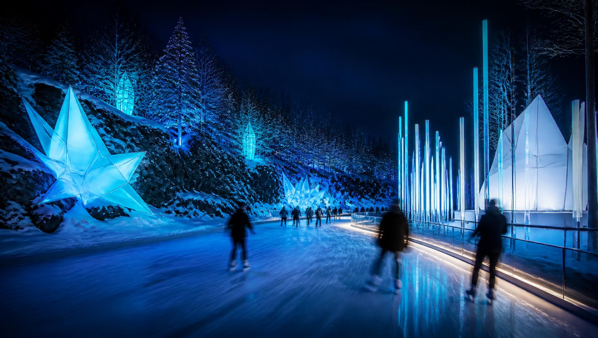 Patineurs sur un parcours de glace illuminé la nuit, entouré de structures lumineuses